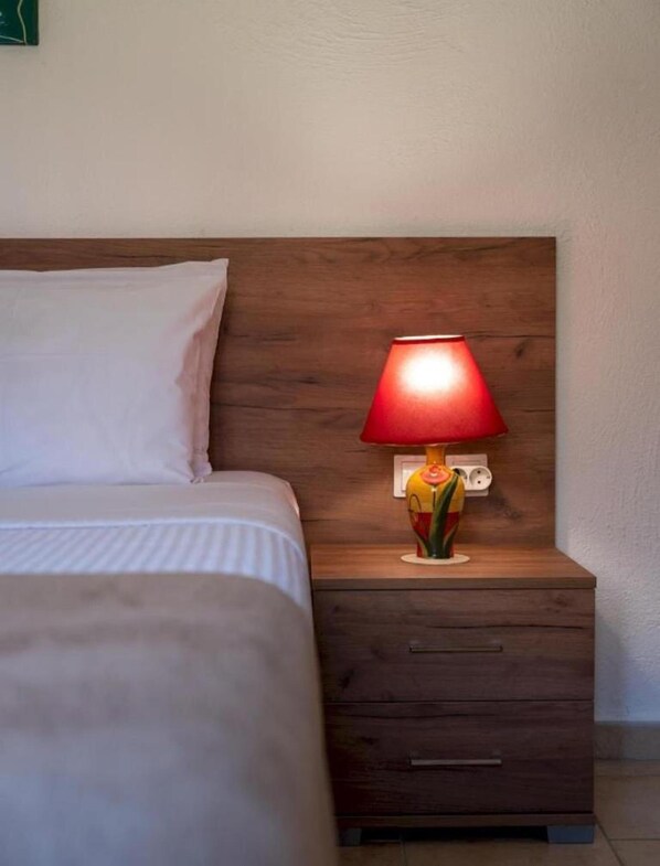A bed with a white pillow and a nightstand with a red lamp. - Atalanti Seaside Junior Suites (Viannos)