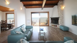 A living room with a wooden ceiling, a fireplace, a TV, and a view of the beach through large sliding doors. - Beach House with 180 degree sea views, 6 Bed, 4 Baths, sleeps 10-12 (La Tranche Sur Mer)