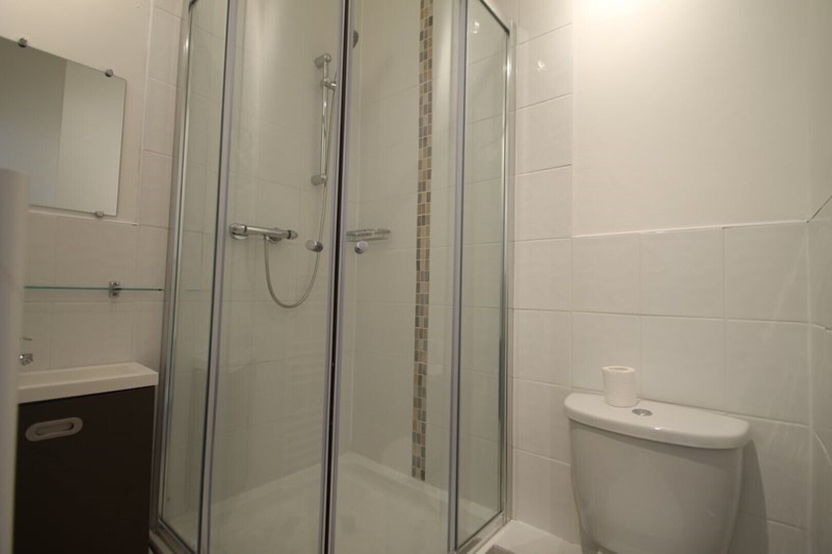 A modern bathroom with a glass-enclosed shower, a toilet, and a glass shelf.