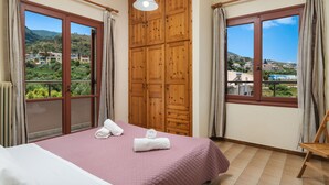 A hotel room with a bed, a wooden wardrobe, and large windows offering a view of the surrounding landscape. - Rustic Garden House, 4BD, 2BA, spacious, peaceful, 10min drive from citycenter (Chania)