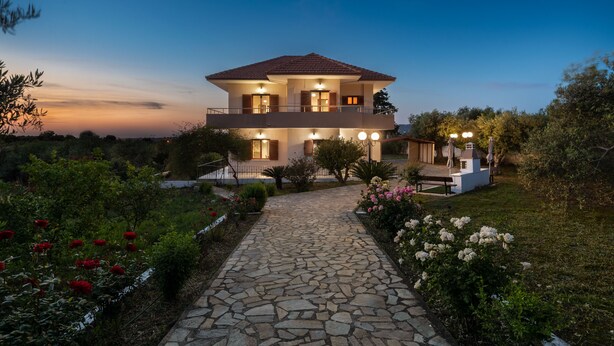 A two-story house with a stone pathway leading to the entrance, surrounded by well-maintained gardens and flowering plants. - Rustic Garden House, 4BD, 2BA, spacious, peaceful, 10min drive from citycenter (Chania)