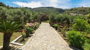 A stone pathway leading to a building surrounded by lush greenery and hills in the background. - Rustic Garden House, 4BD, 2BA, spacious, peaceful, 10min drive from citycenter (Chania)