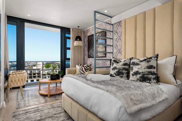 Une chambre moderne avec un grand lit, un balcon offrant une belle vue et une échelle de style industriel.