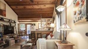 Un salon chaleureux avec un plafond en bois, une télévision, un canapé et un coin repas comprenant des chaises et une table.
