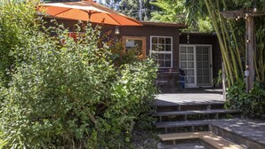 Une cabane en bois dotée d’une terrasse couverte, entourée d’une végétation luxuriante et d’arbres.