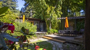 Un espace patio doté d’une terrasse en bois, de sièges d’extérieur et d’une pergola surmontée d’un parasol orange.