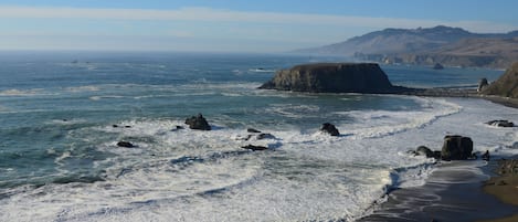 A coastal landscape with a sandy beach, rocky outcrops, and a clear view of the ocean.