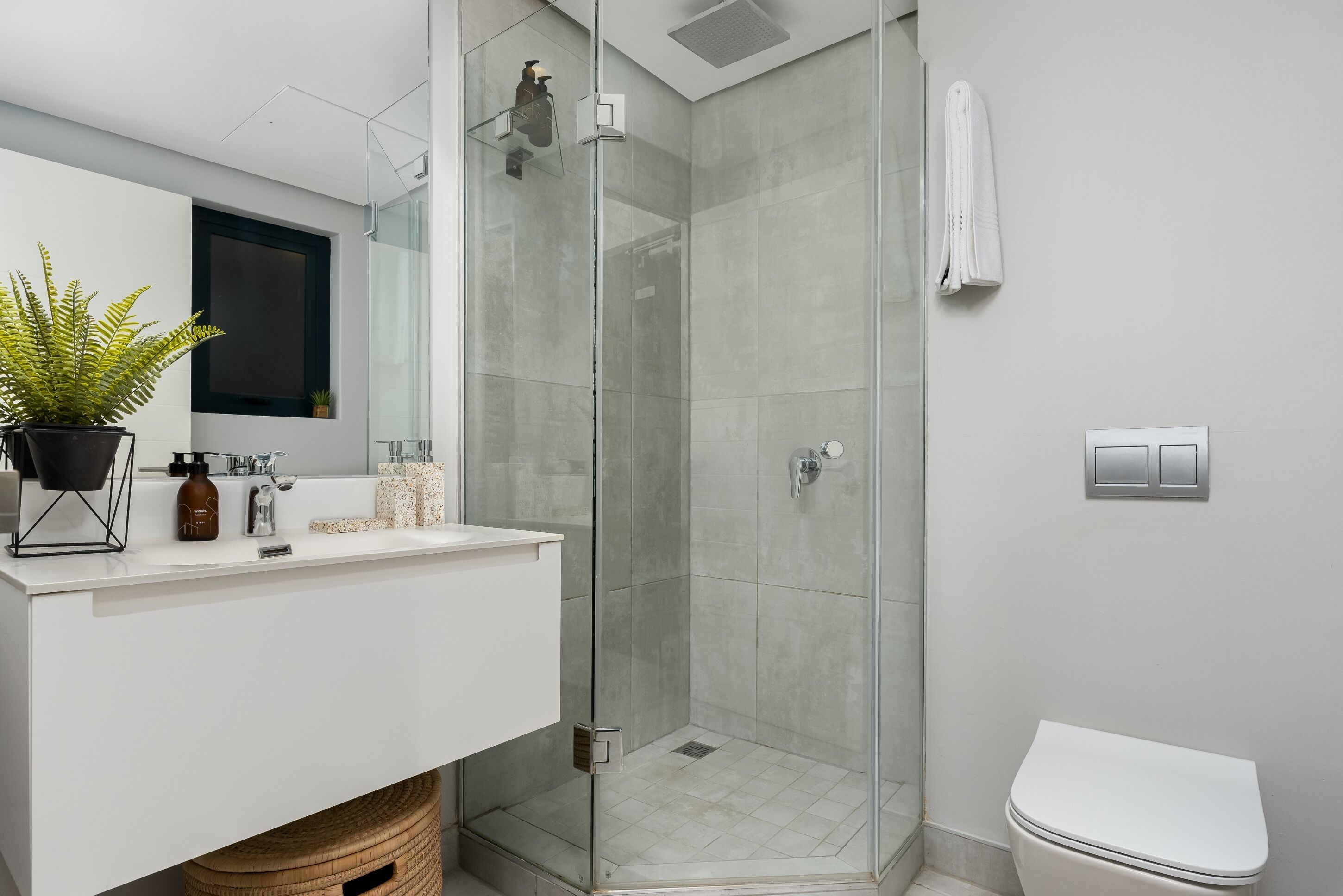 Een moderne badkamer met een douchecabine van glas, een wit wastafelmeubel met spiegel, en een wit toilet.