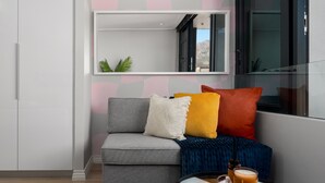 Una sala de estar moderna con un sofá gris, cojines coloridos, un plaid azul, una mesa de centro redonda con tapa de cristal y vistas a una montaña a través de una ventana.