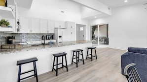 Cocina moderna con armarios blancos, una isla de mármol con taburetes y un comedor con sofá azul.