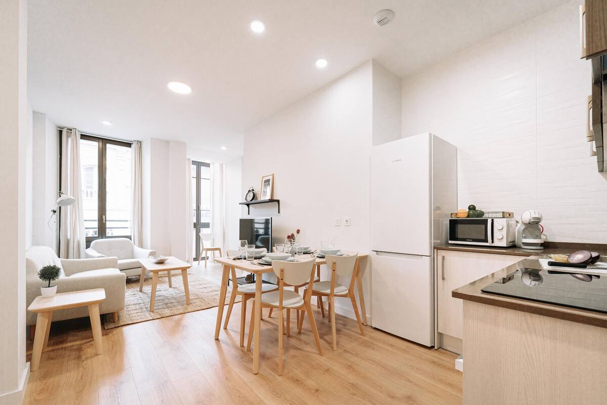 A modern kitchen with wooden flooring, white cabinetry, and a dining area with a table and chairs.