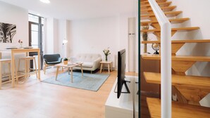 A modern living room with a sofa, coffee table, and TV, a staircase with wooden steps, and a dining area with a table and chairs. - San Bernardo 19 (Aviles)