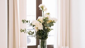 A dining table set with white plates, bowls, and cutlery, surrounded by white chairs, with a vase of white flowers in the center. - San Bernardo 19 (Aviles)
