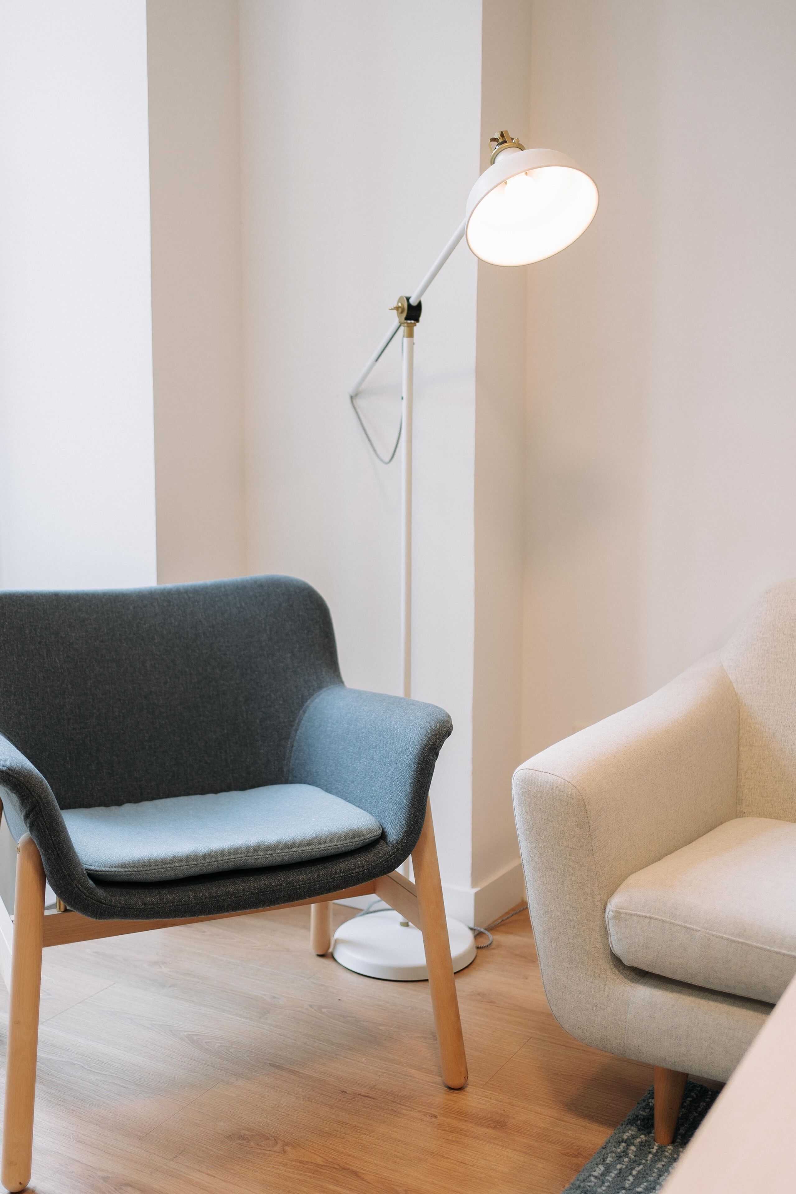 Una habitación con un sillón tapizado en gris, una lámpara de pie blanca y un sillón de color claro.