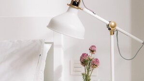 A white bedside table with a white lamp, a vase with pink flowers, and a glass of water. - San Bernardo 19 (Aviles)