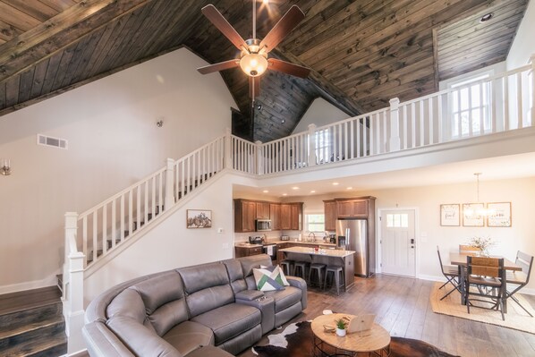 A spacious living area with a curved gray leather sofa, a round coffee table, and a ceiling fan. - Ellijay GA Cozy Cabin Escape, Hot Tub, Arcade & Game Room sleeps 9 (Ellijay)