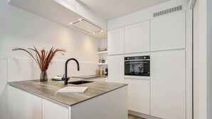 A modern kitchen with white cabinetry, a central island, a black faucet, and a built-in oven. - Port Orion - brand new ground floor flat with pool (Nieuwpoort)