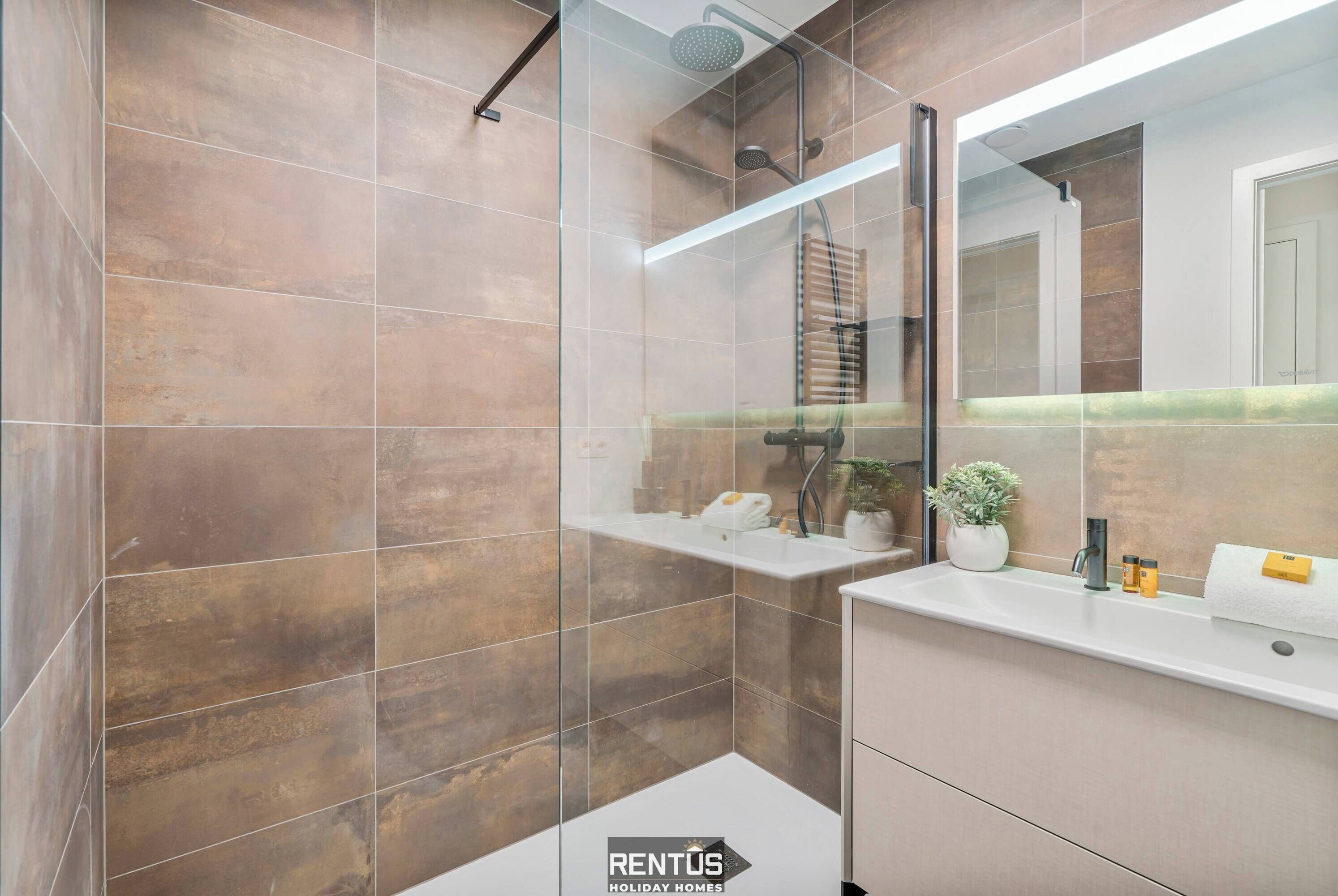 Un bagno moderno con doccia a vetro, lavandino bianco e specchio sopra.