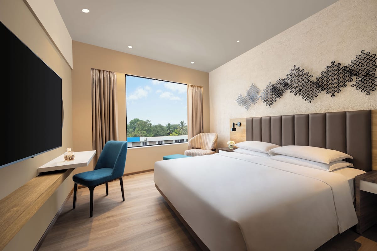 A modern hotel room with a large bed, a desk with a chair, a TV, and a view of the outdoors.