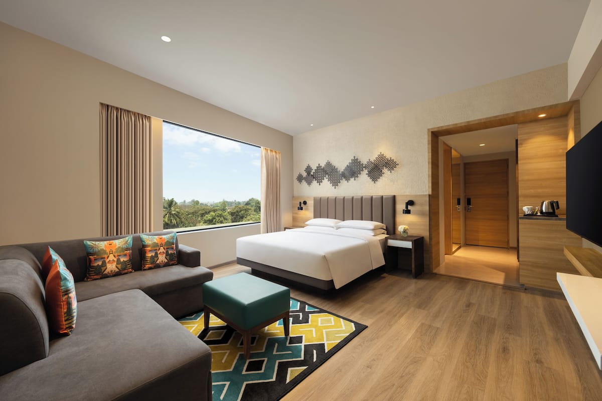A modern hotel room with a large bed, a sofa, a coffee table, and a view of the outdoors.