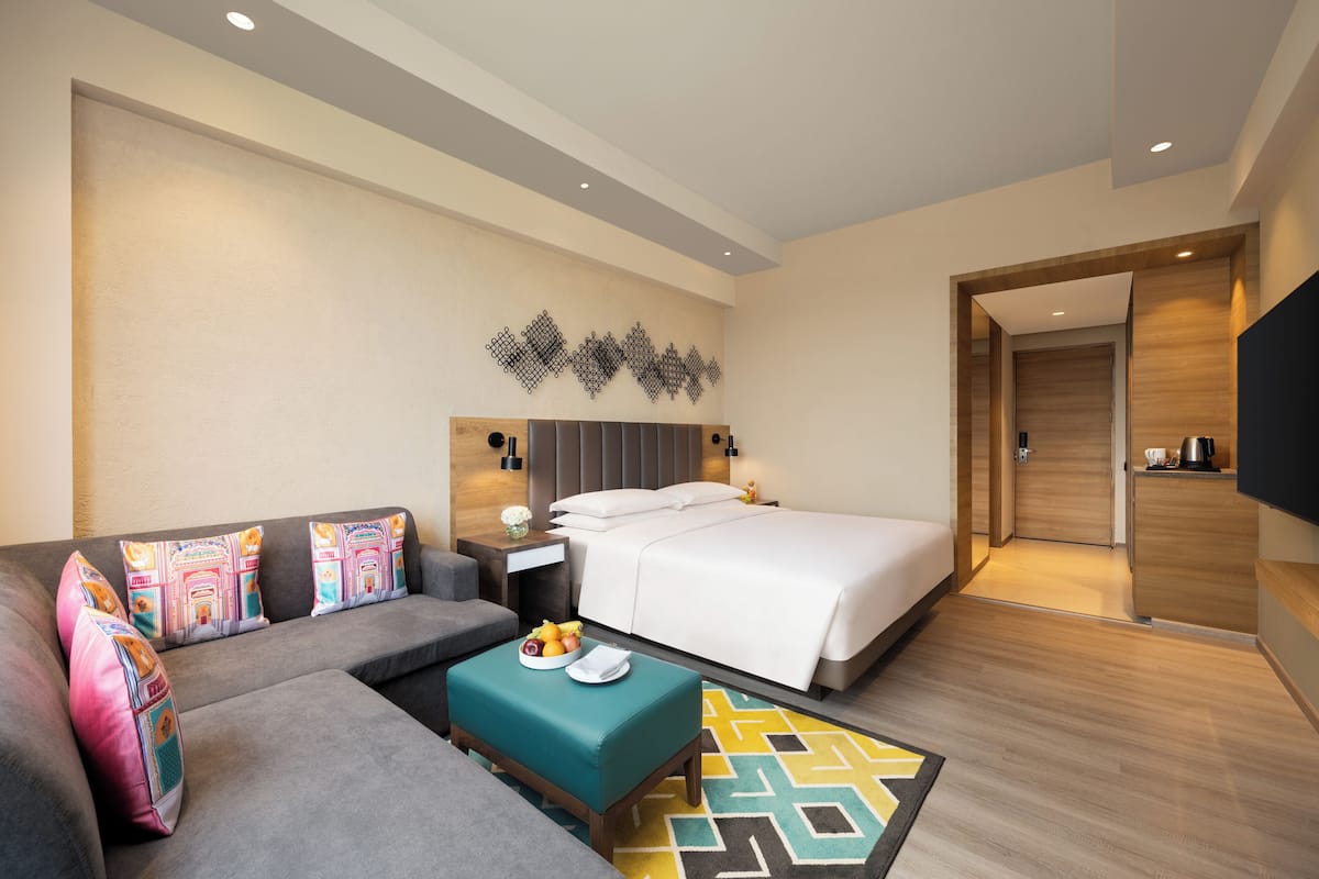 A modern hotel room with a bed, sofa, bedside table, and a TV.