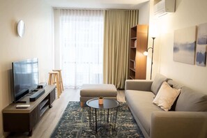 Una sala moderna con un televisor de pantalla plana, un sofá, una mesa de centro y una estantería.