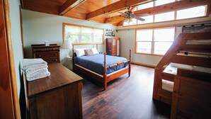 Een slaapkamer met een houten bed, een dressoir, een nachtkastje en een raam met uitzicht op bomen.