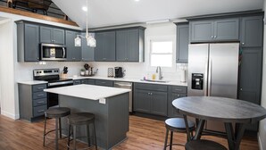 Una cocina moderna con gabinetes grises, un refrigerador de acero inoxidable, un horno empotrado y una isla grande con taburetes.