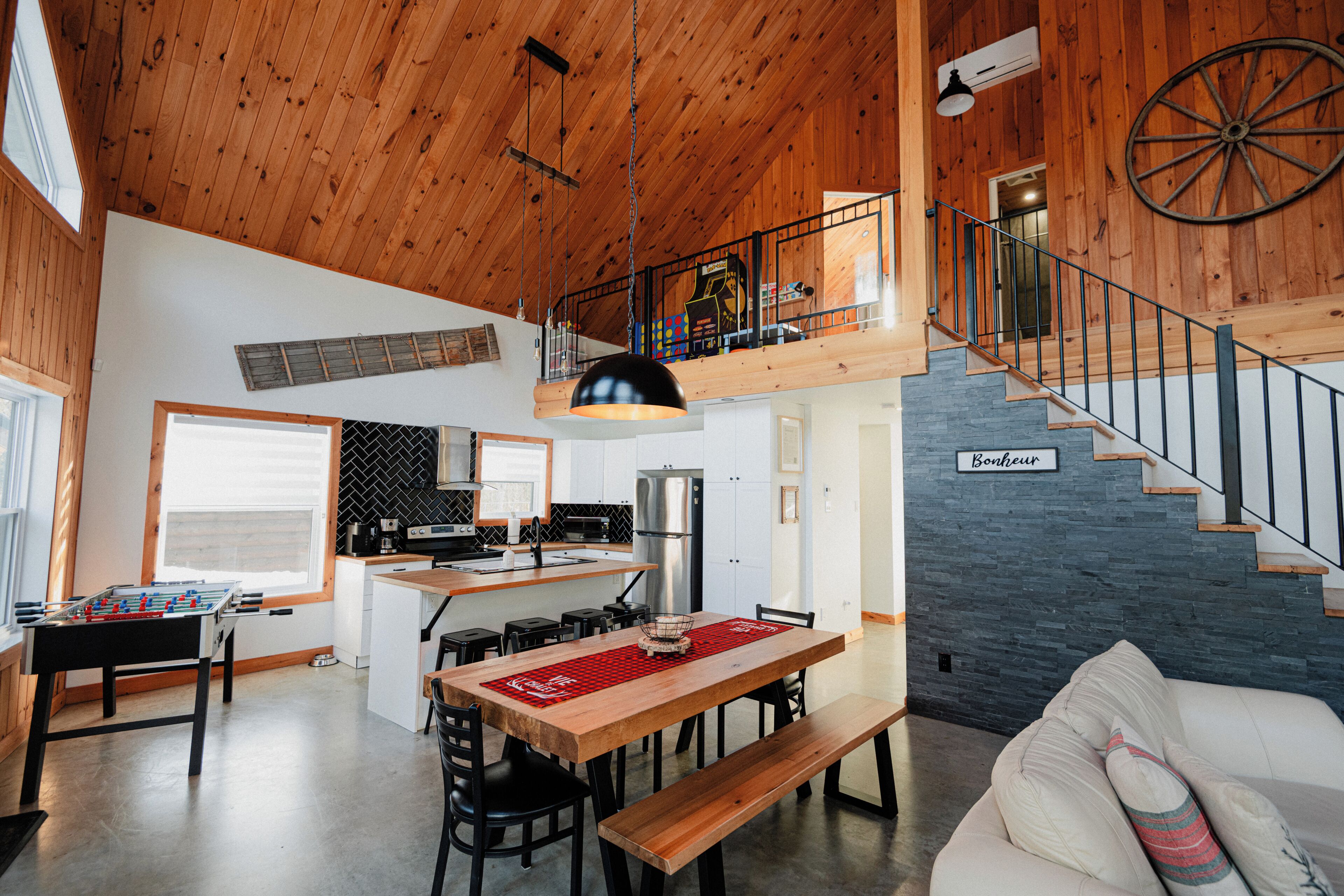 Un vaste espace de vie doté d’un plafond en bois, d’une table à manger avec des chaises, d’un canapé et d’un escalier menant à un niveau supérieur.