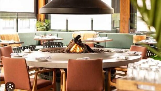 A restaurant interior with round tables, chairs, and a central fire feature. - "Inspired Elegance" at Tamarack Lodge (Canmore)