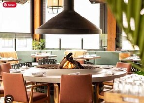 A restaurant interior with round tables, chairs, and a central fire feature.