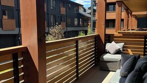 A balcony with wooden railings, a grey sofa with cushions, and a view of a mountain and buildings in the background. - "Inspired Elegance" at Tamarack Lodge (Canmore)