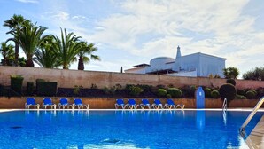 A swimming pool with blue water, surrounded by lounge chairs and palm trees.