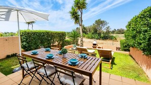 An outdoor dining area with a wooden table, blue plates, and a white umbrella.