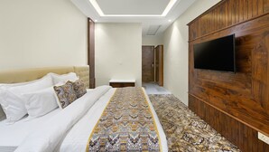 A bedroom with a bed, a TV mounted on the wall, and a ceiling fan. - Hotel Paras (Dera Bassi)
