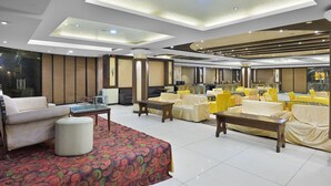 A spacious hotel lobby with a modern design, featuring a large seating area with sofas and tables, a patterned rug, and a large mirror reflecting the room. - Hotel Paras (Dera Bassi)