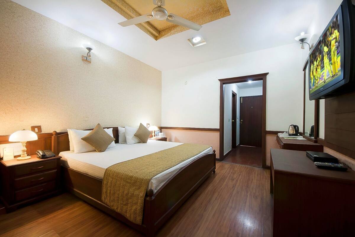 Habitación de hotel con una cama grande, mesitas de noche, un escritorio, un televisor de pantalla plana y una puerta que da a otra habitación.
