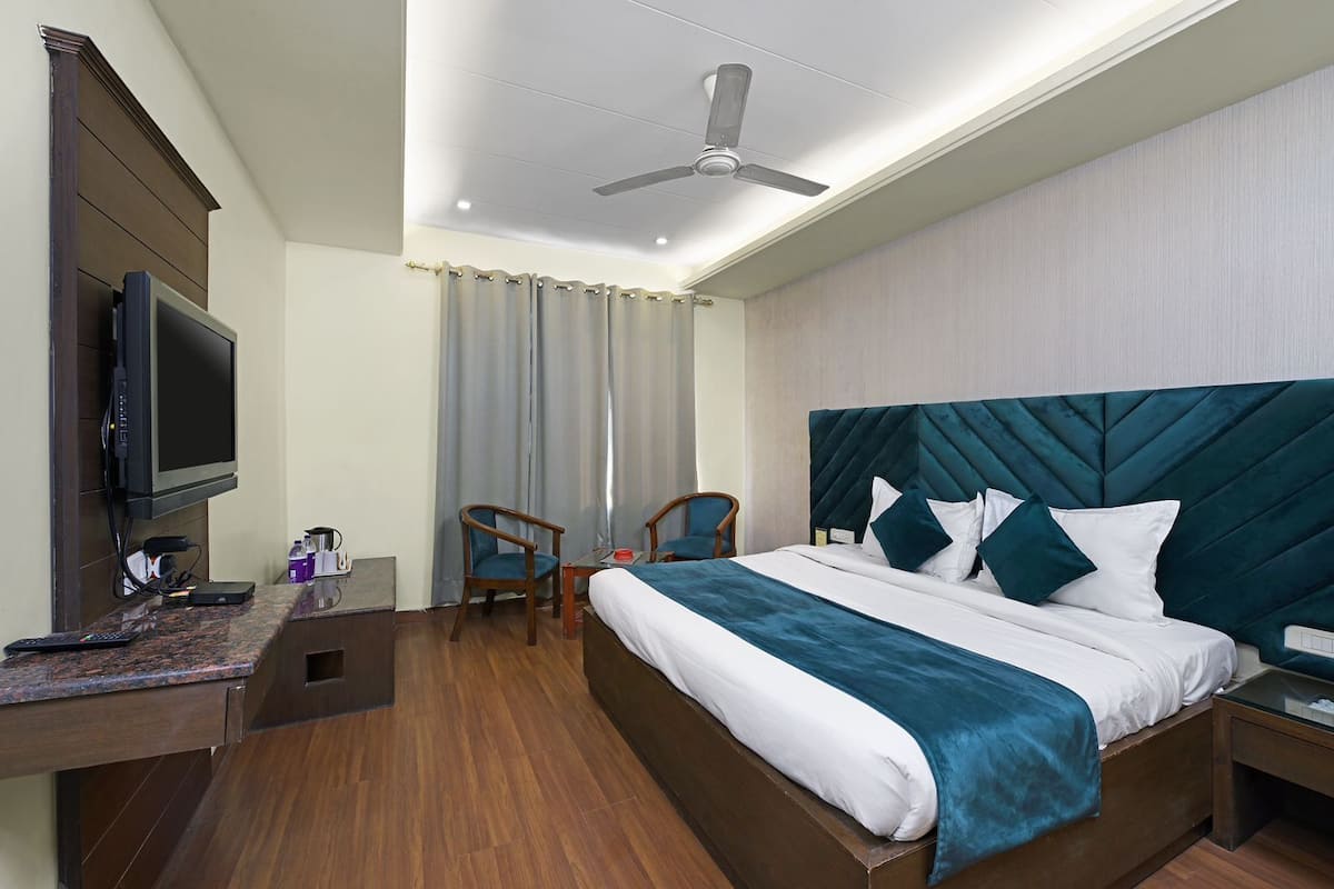 Una habitación de hotel con cama, escritorio con televisor, una silla y ventilador de techo.