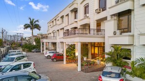 A hotel with a covered outdoor area, multiple parked cars, and a palm tree. - Hotel Paras (Dera Bassi)