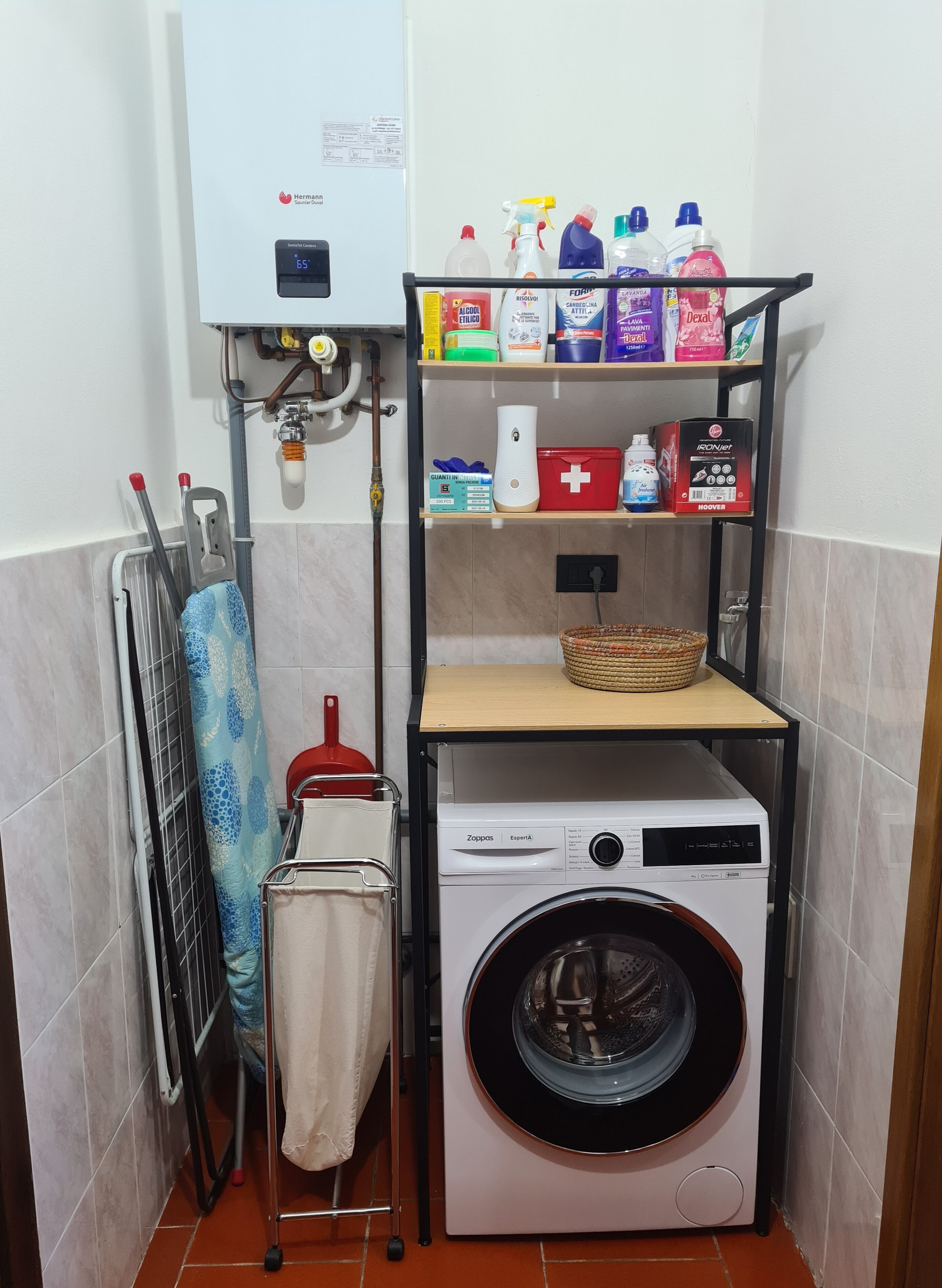 A compact laundry area with a washing machine, a drying rack, and shelves stocked with cleaning supplies.