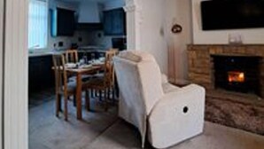 A living room with a fireplace, a dining area with a table and chairs, and a kitchen visible through an archway. - Immaculate 2-bed Cottage - Free Wifi (Bridlington)