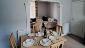 A dining area with a table set for four, a sofa in the background, and a white door. - Immaculate 2-bed Cottage - Free Wifi (Bridlington)
