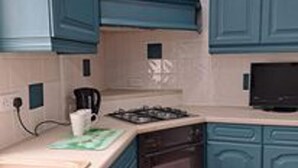 A kitchen with teal cabinets, a stove, a microwave, and a coffee maker. - Immaculate 2-bed Cottage - Free Wifi (Bridlington)