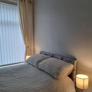 Ein Hotelzimmer mit einem Bett, einem Nachttisch, einer Lampe und einem Fenster mit Vorhängen.
