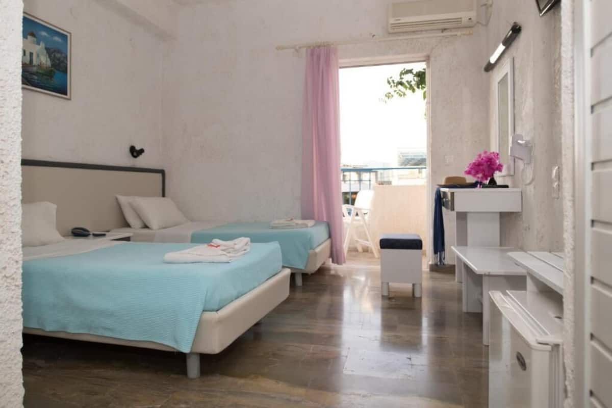Quarto com duas camas, uma varanda pequena, uma pia branca e um quadro na parede.