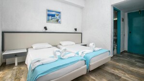 A hotel room with two beds, a nightstand, a wall-mounted picture, and a teal door. - Gorgona Hotel (Malevizi)
