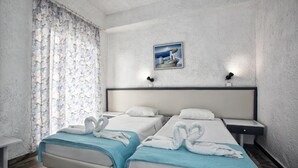 A hotel room with two beds, a small bedside table, a nightstand, a picture on the wall, and a window with curtains. - Gorgona Hotel (Malevizi)