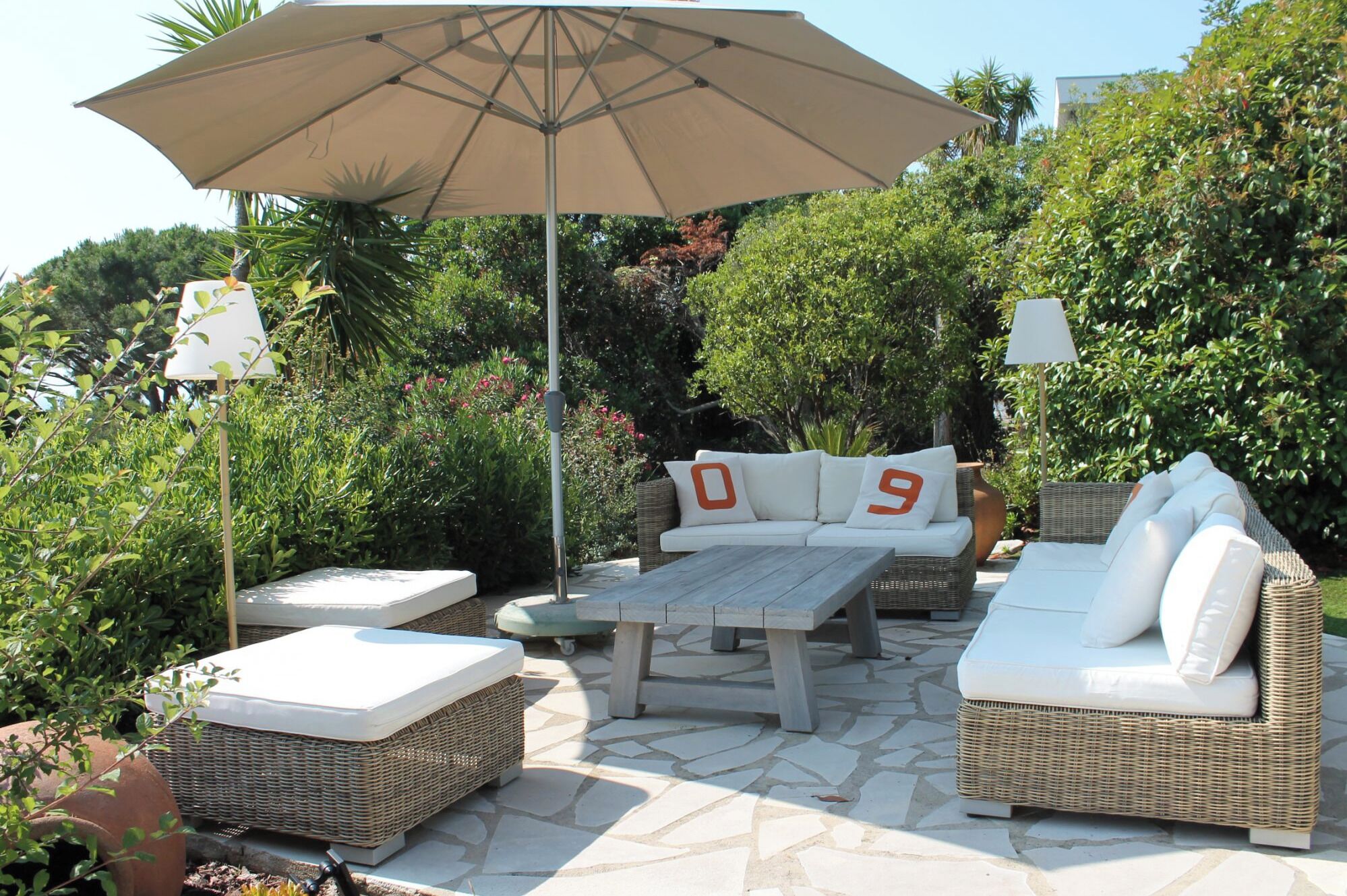 An outdoor patio area with wicker furniture, including sofas and a table, under a large umbrella.