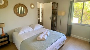 A neatly made bed with white linens and rolled towels, a bedside table with a lamp, and a large window with curtains.