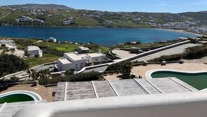 Ein Küstenresort mit moderner Architektur, einem Schwimmbad und Blick auf das Meer und die umliegenden Hügel.